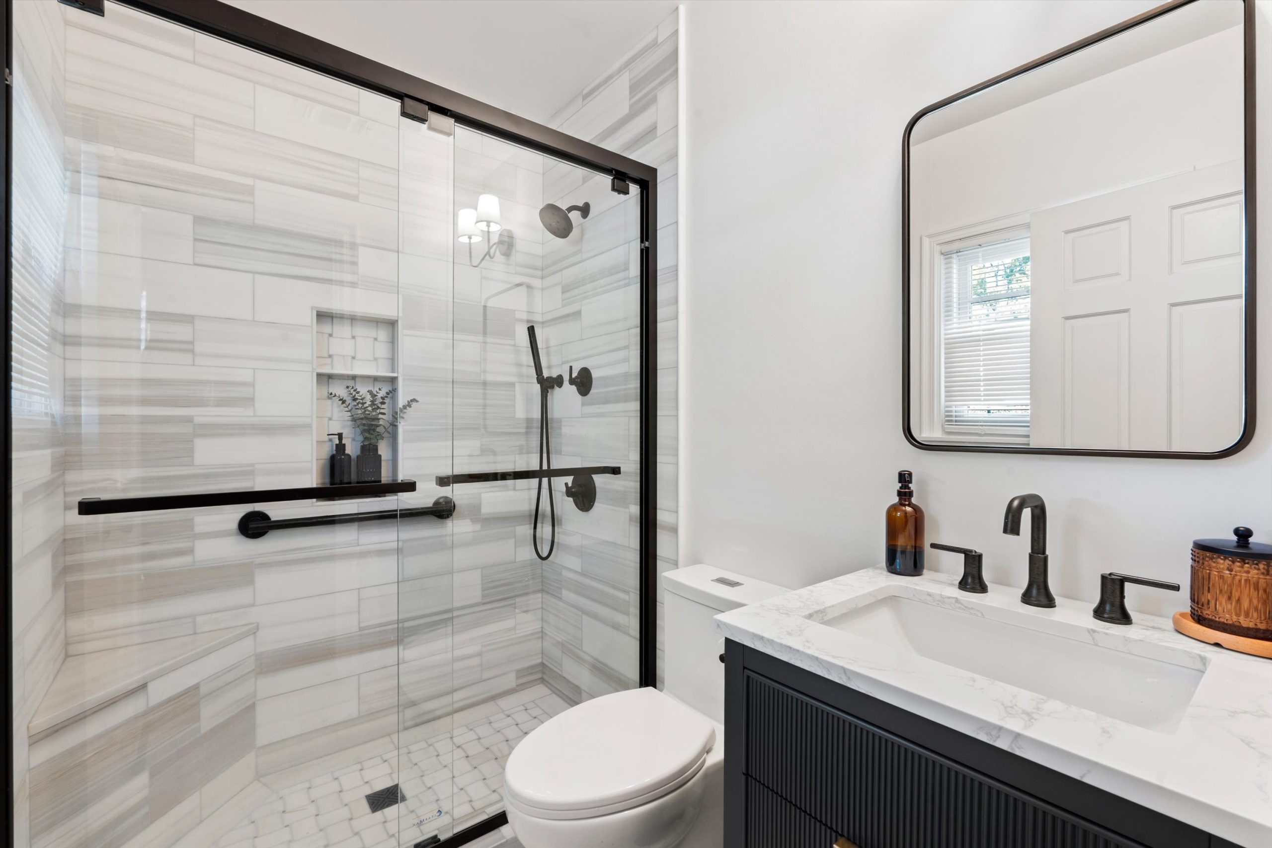 Modern bathroom remodel with black-framed glass shower enclosure, marble tile walls, and dark wood vanity
